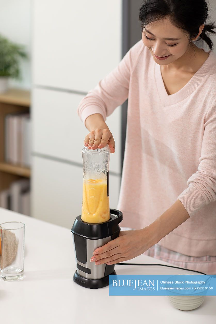Happy young Chinese woman making juice at home