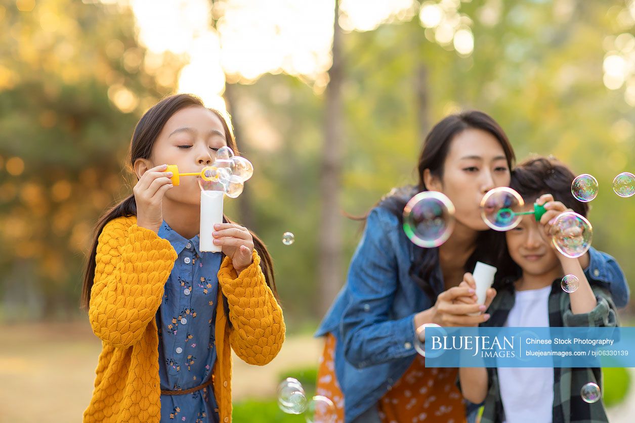 Happy young Chinese family blowing bubbles in park