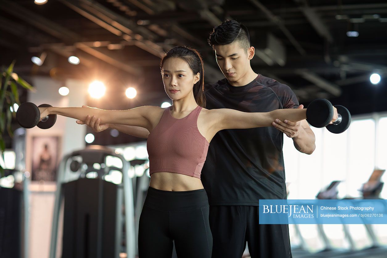 Young Chinese woman working out with personal trainer at gym