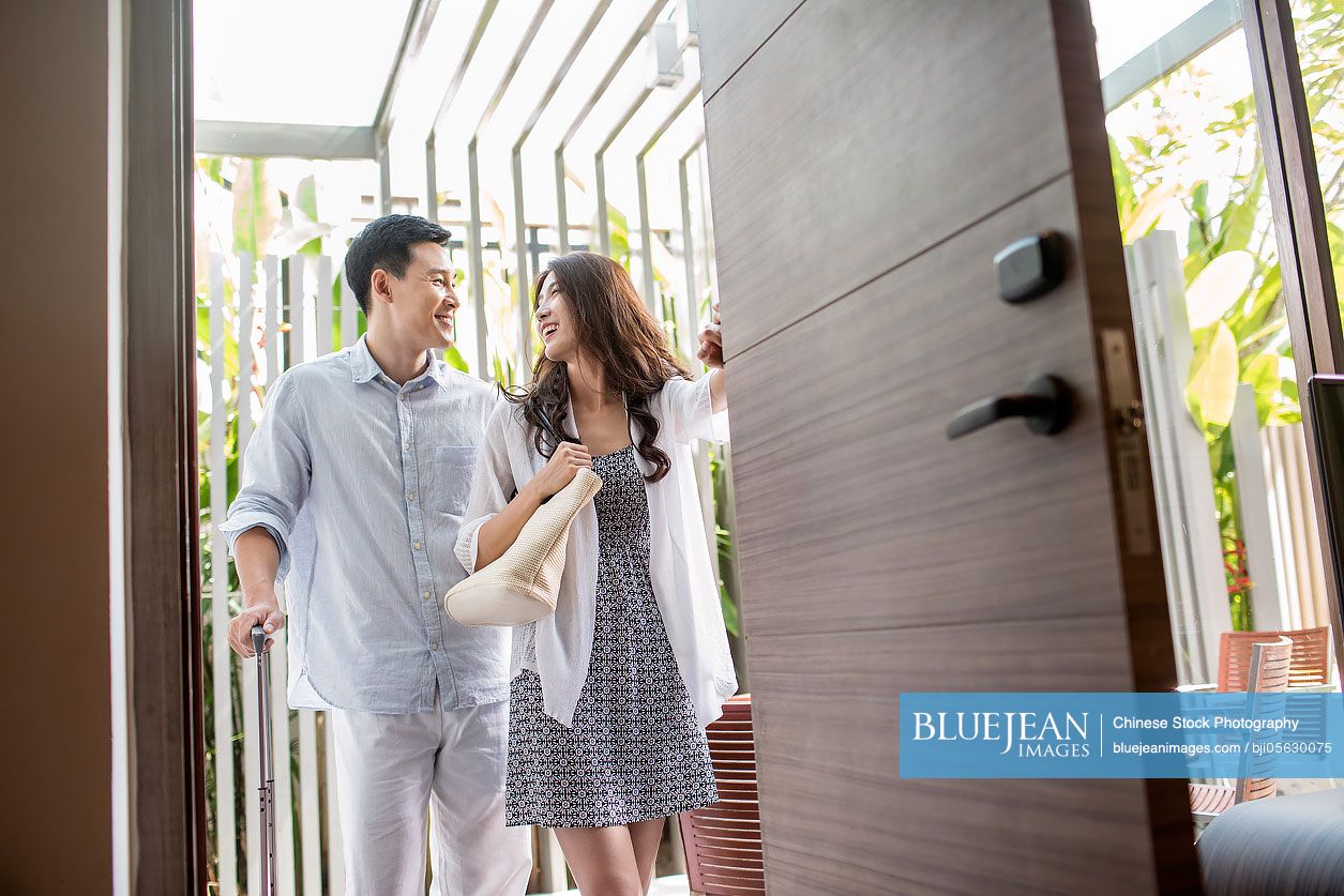 Happy young Chinese couple entering hotel room with suitcase