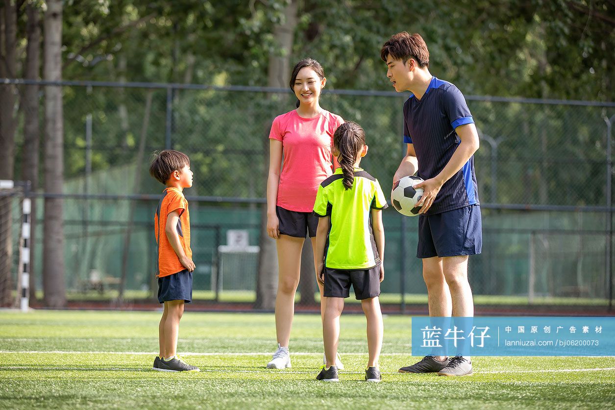 快乐的年轻家庭在足球场踢足球