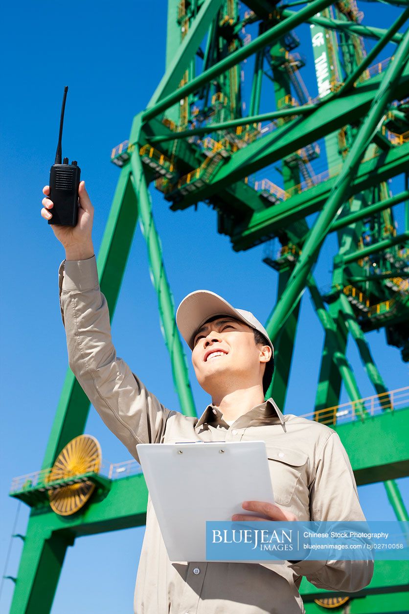 Male Chinese shipping industry worker with walkie-talkie pointing