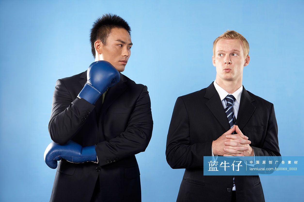 穿职业装的亚洲人戴拳击手套,穿职业装的白人在一旁露出害怕的神情-蓝  image