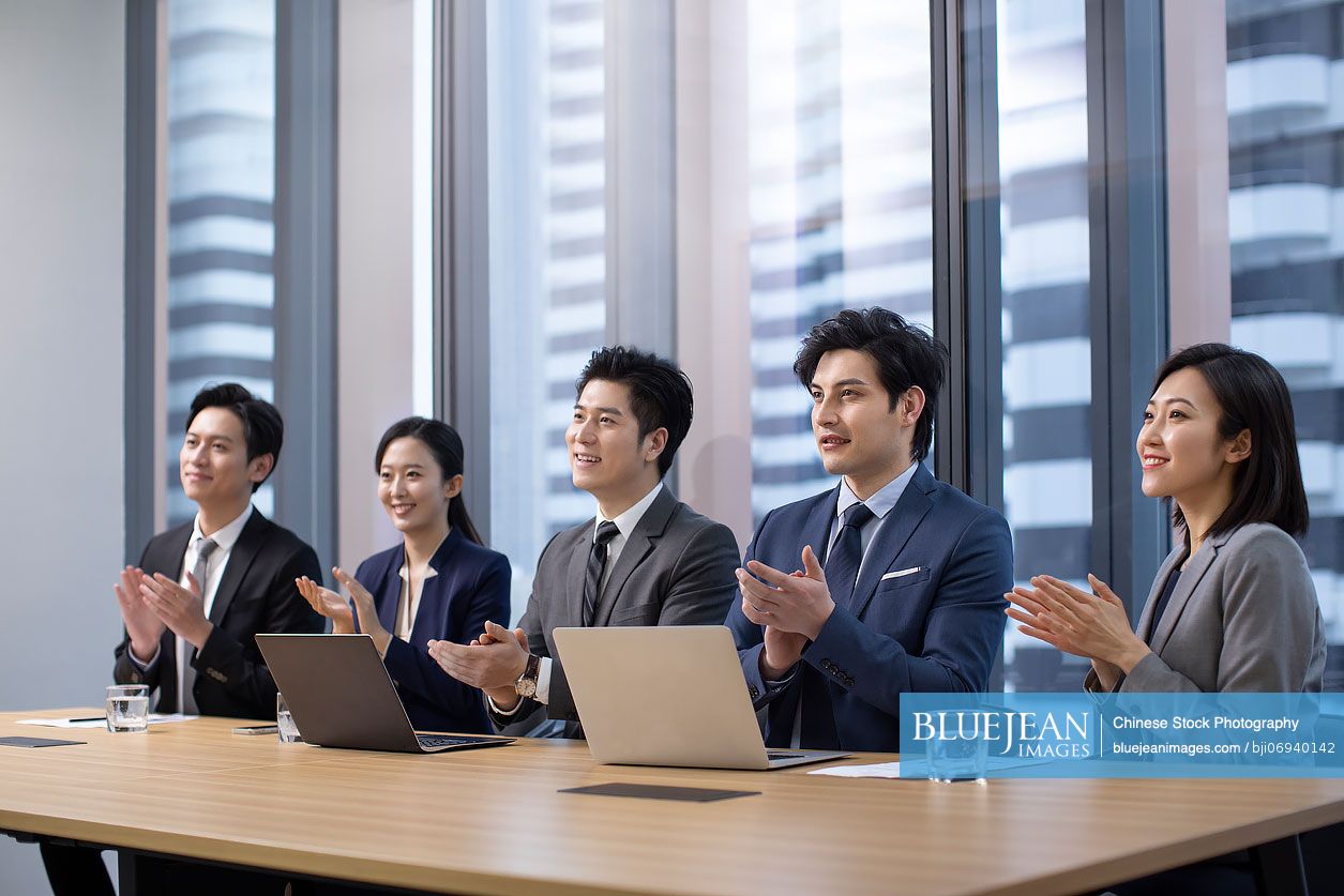 Cheerful Chinese business people applauding in meeting room