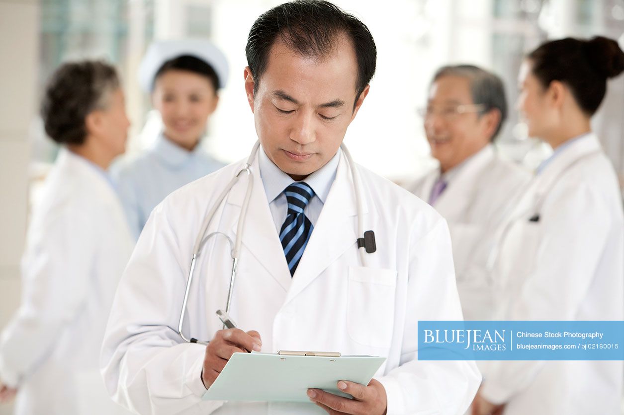 Chinese doctor with clipboard with doctors and nurse in background