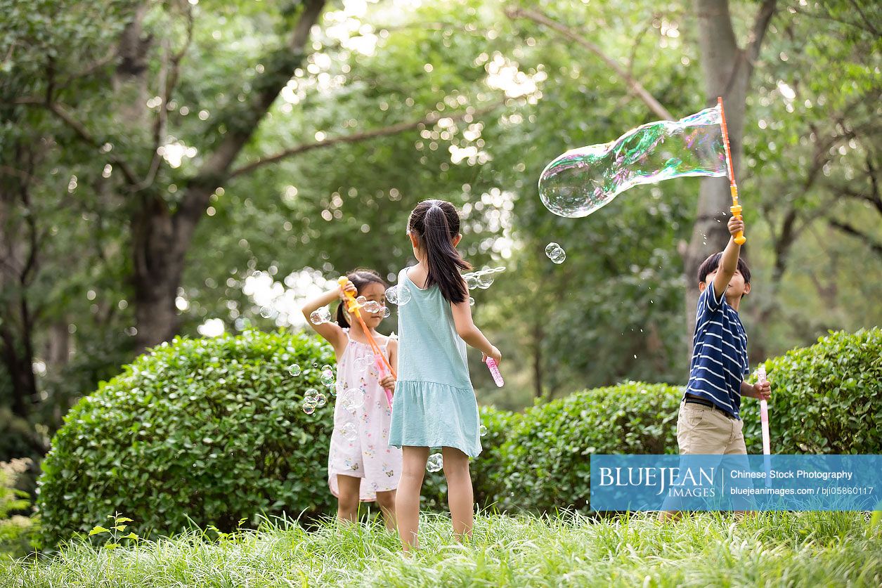 Three Chinese children blowing bubbles on grass