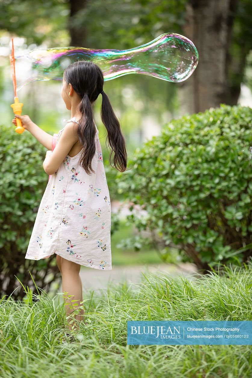 Little Chinese girl blowing bubbles on grass