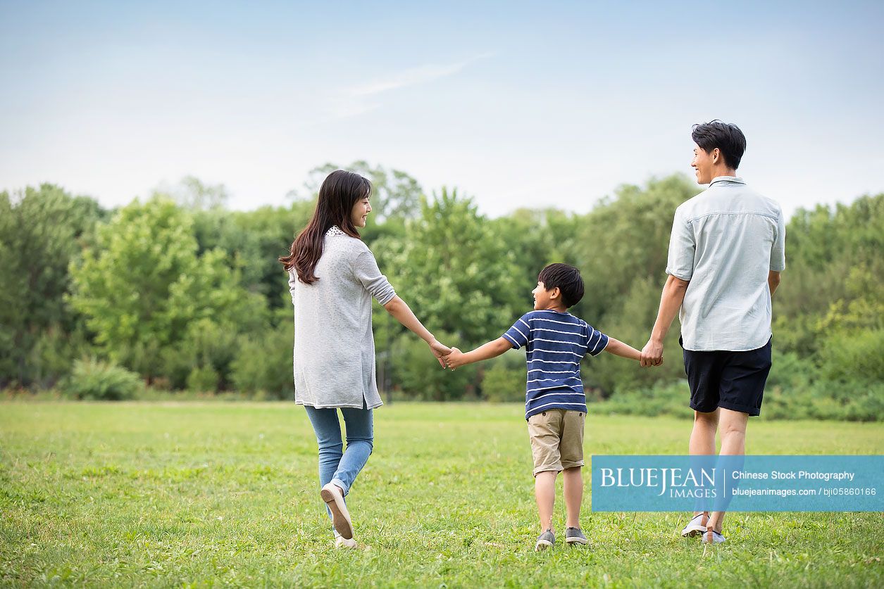 Happy young Chinese family walking on grass