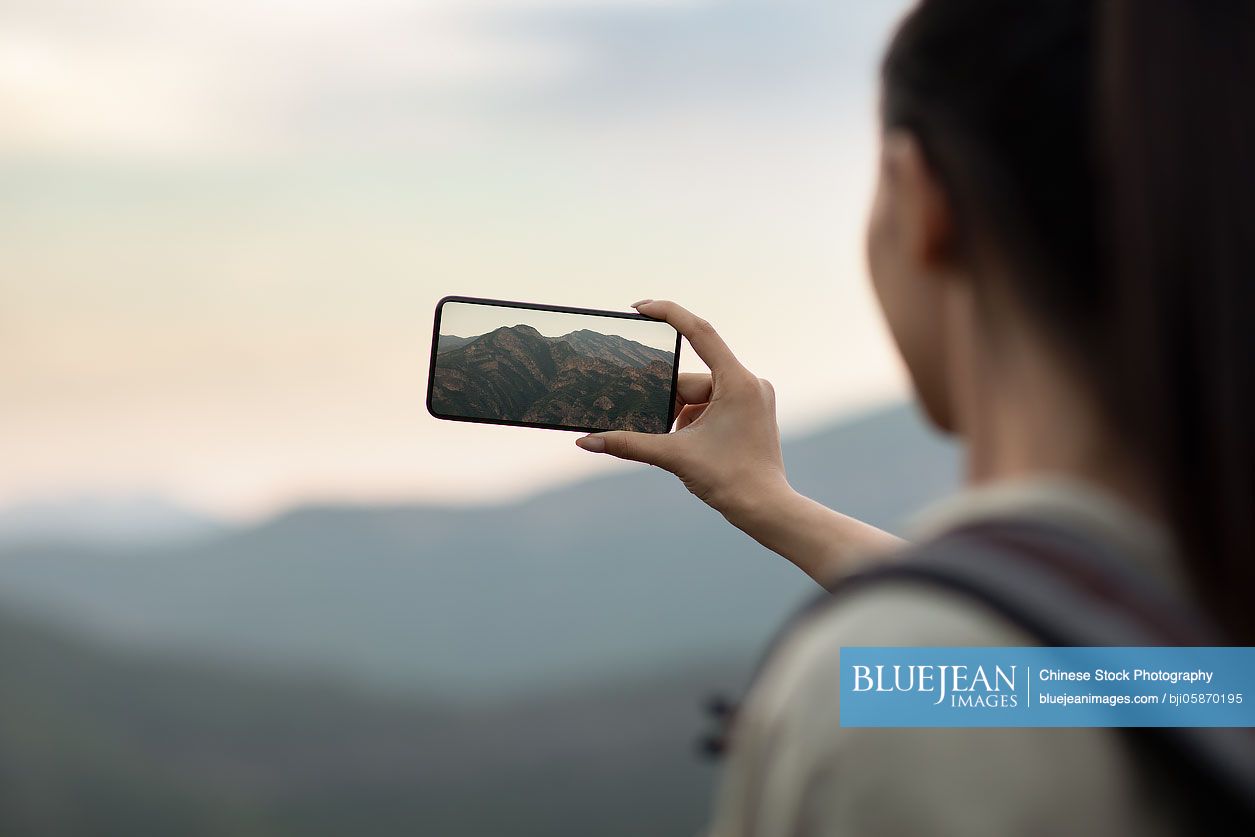 Young Chinese woman taking photos with smartphone outdoors