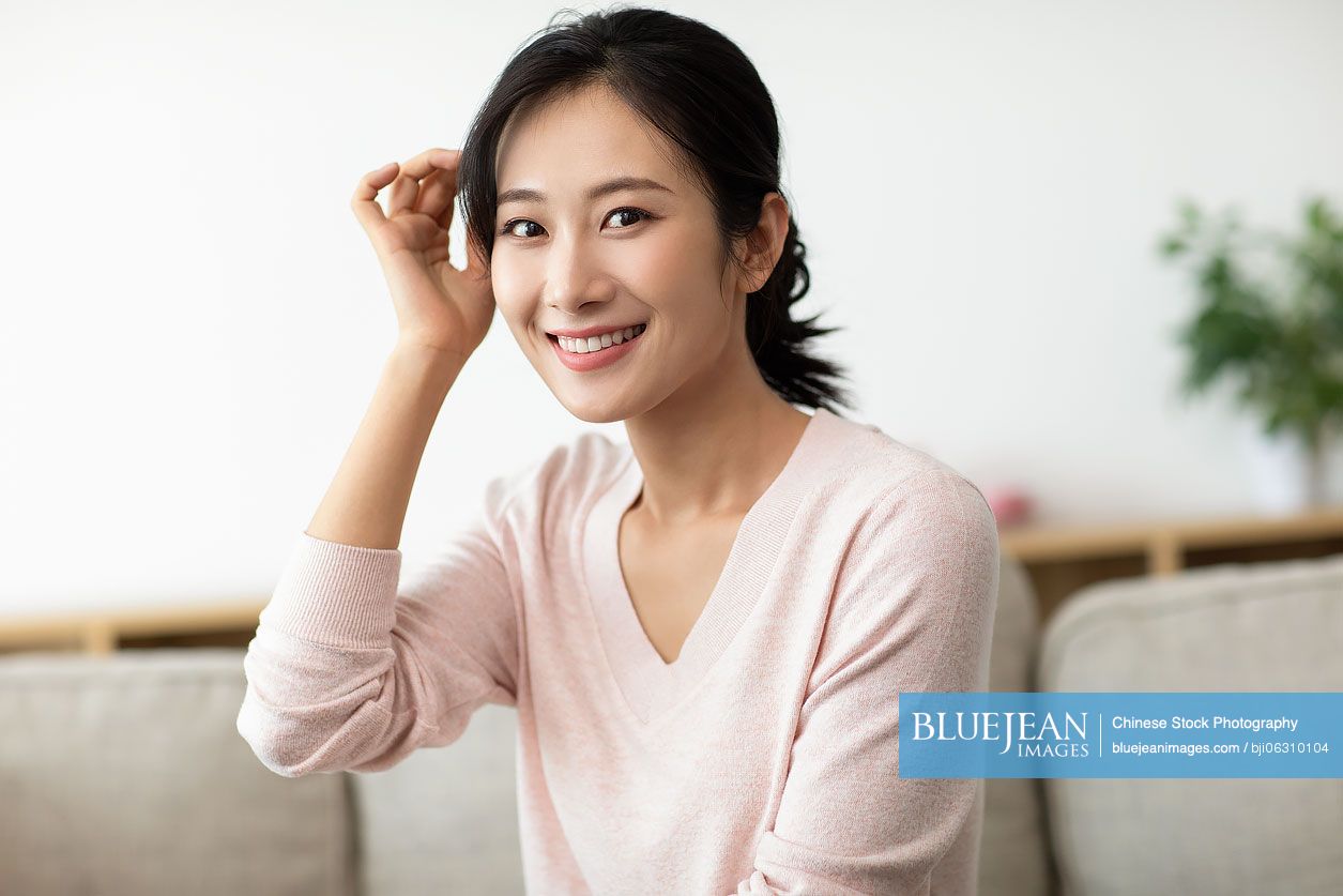Happy young Chinese woman sitting on sofa