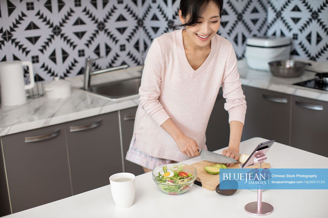 Happy young Chinese woman cooking in kitchen