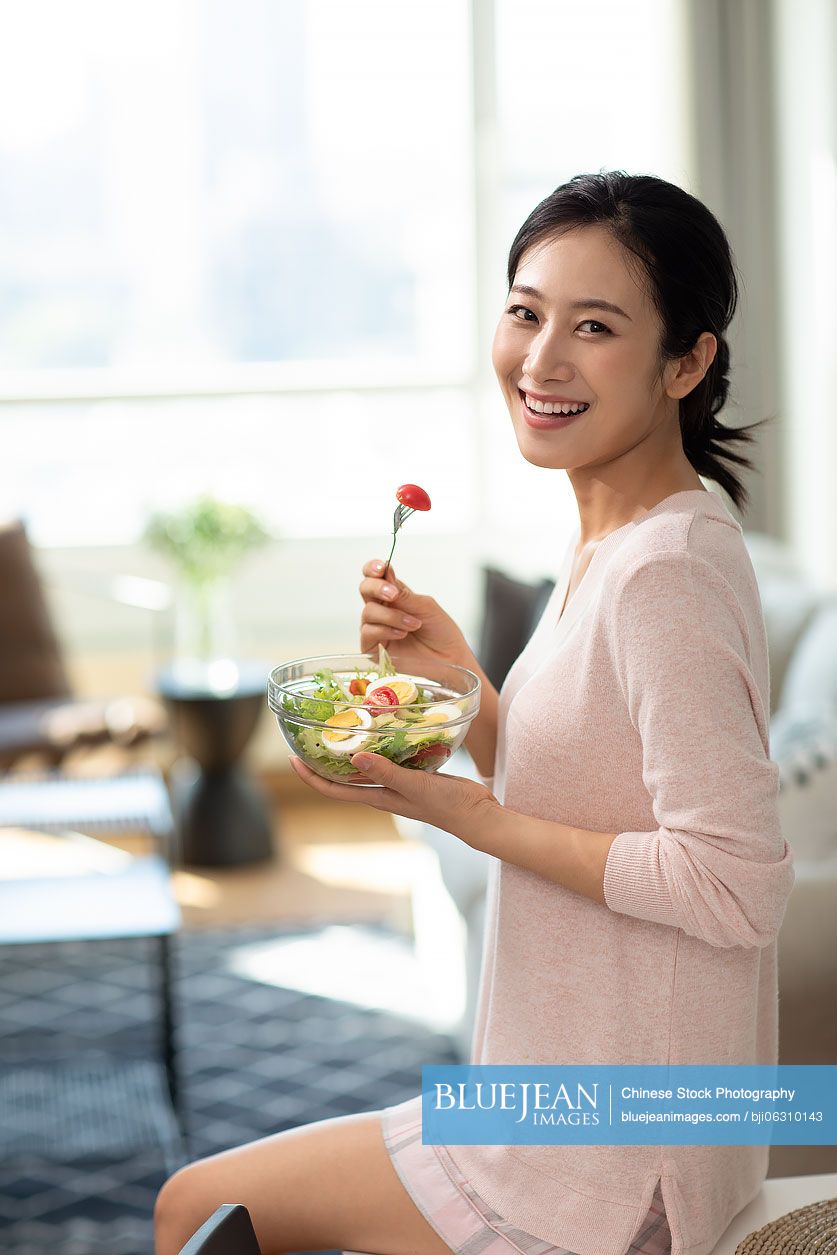 Happy young Chinese woman eating salad at home