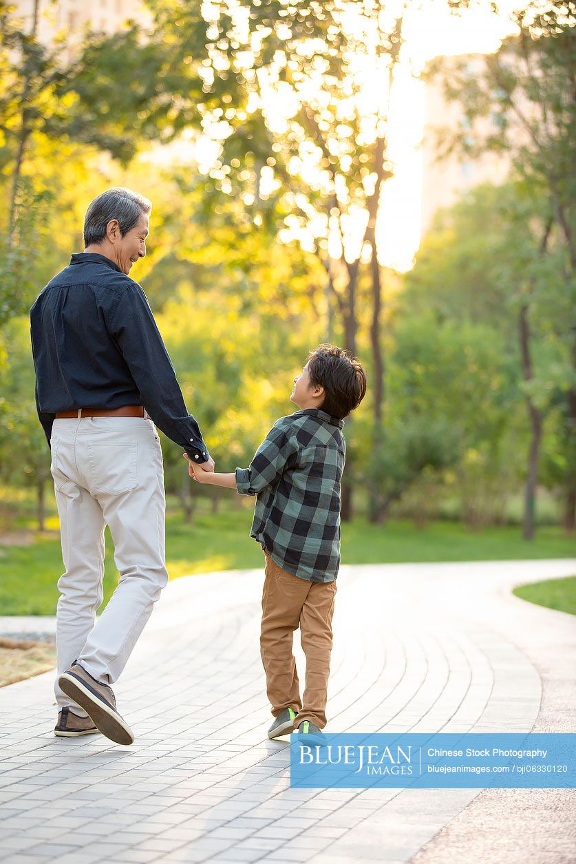 Happy Chinese grandfather and grandson walking in park