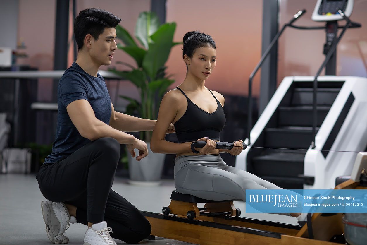 Young Chinese woman working out with personal trainer at gym