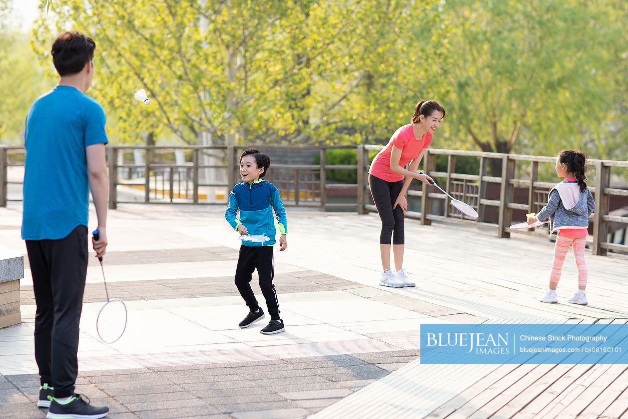 Happy young Chinese family playing badminton in park