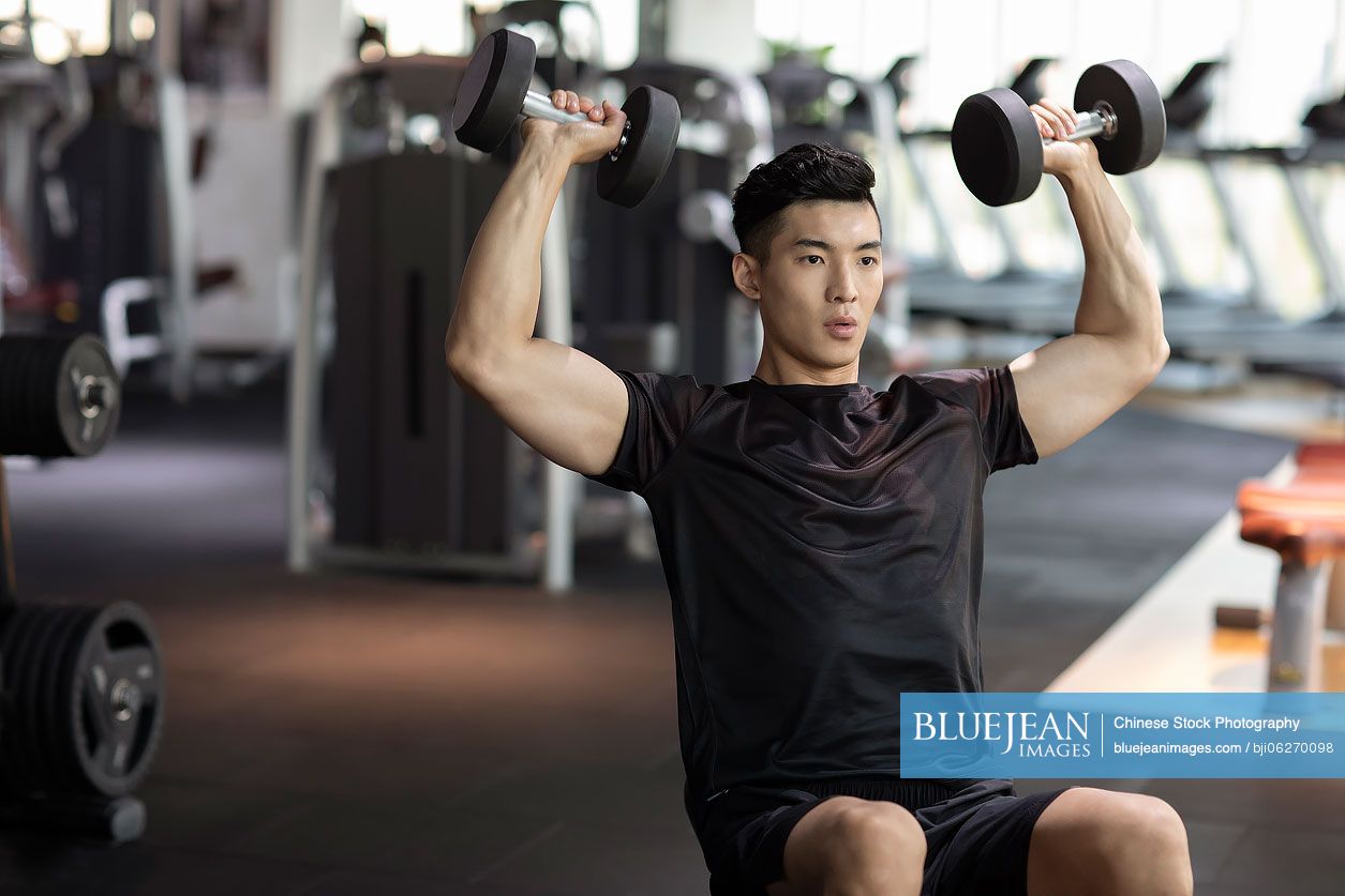 Young Chinese man working out with dumbbell at gym