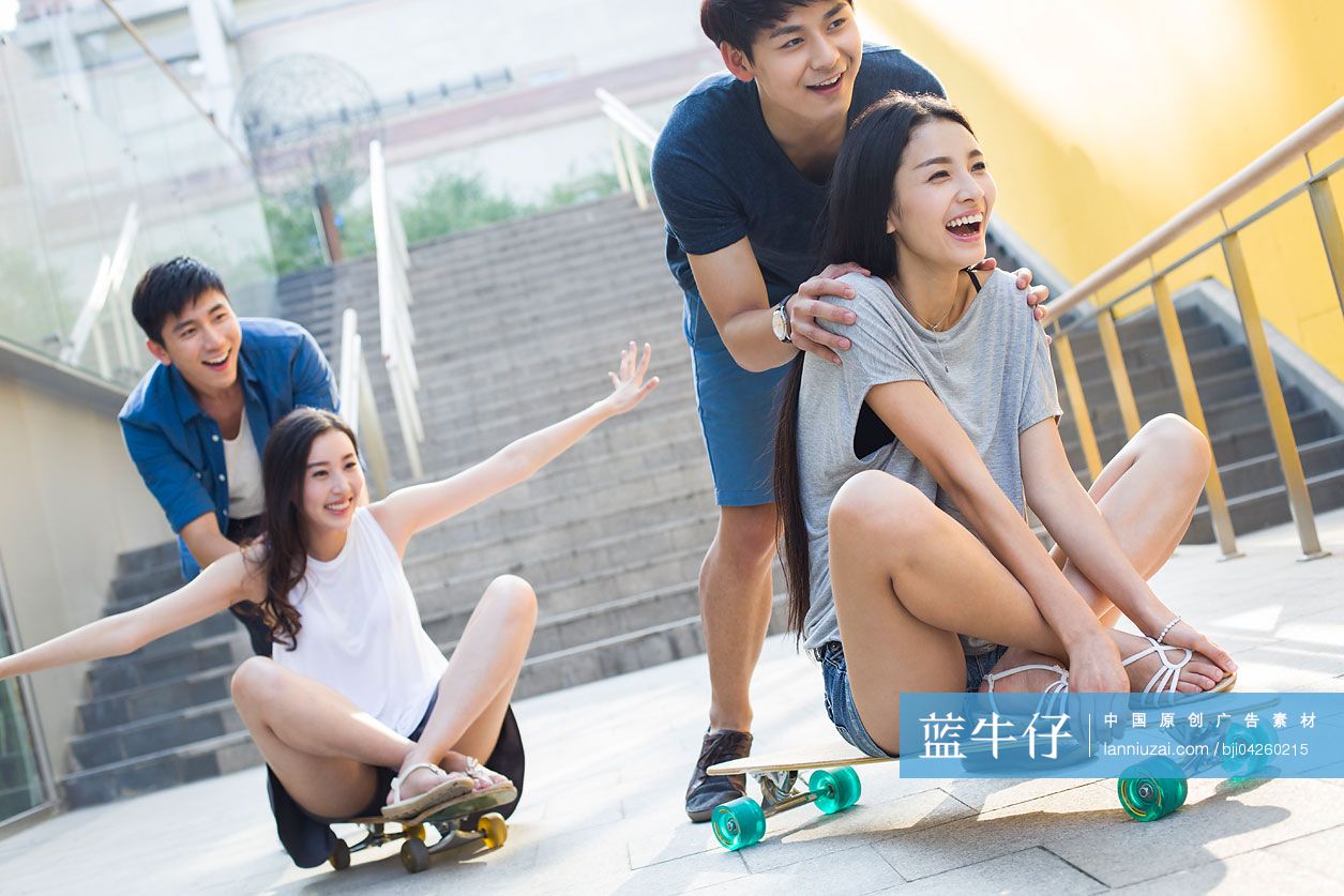 年轻男子向前推着坐在滑板上的女友