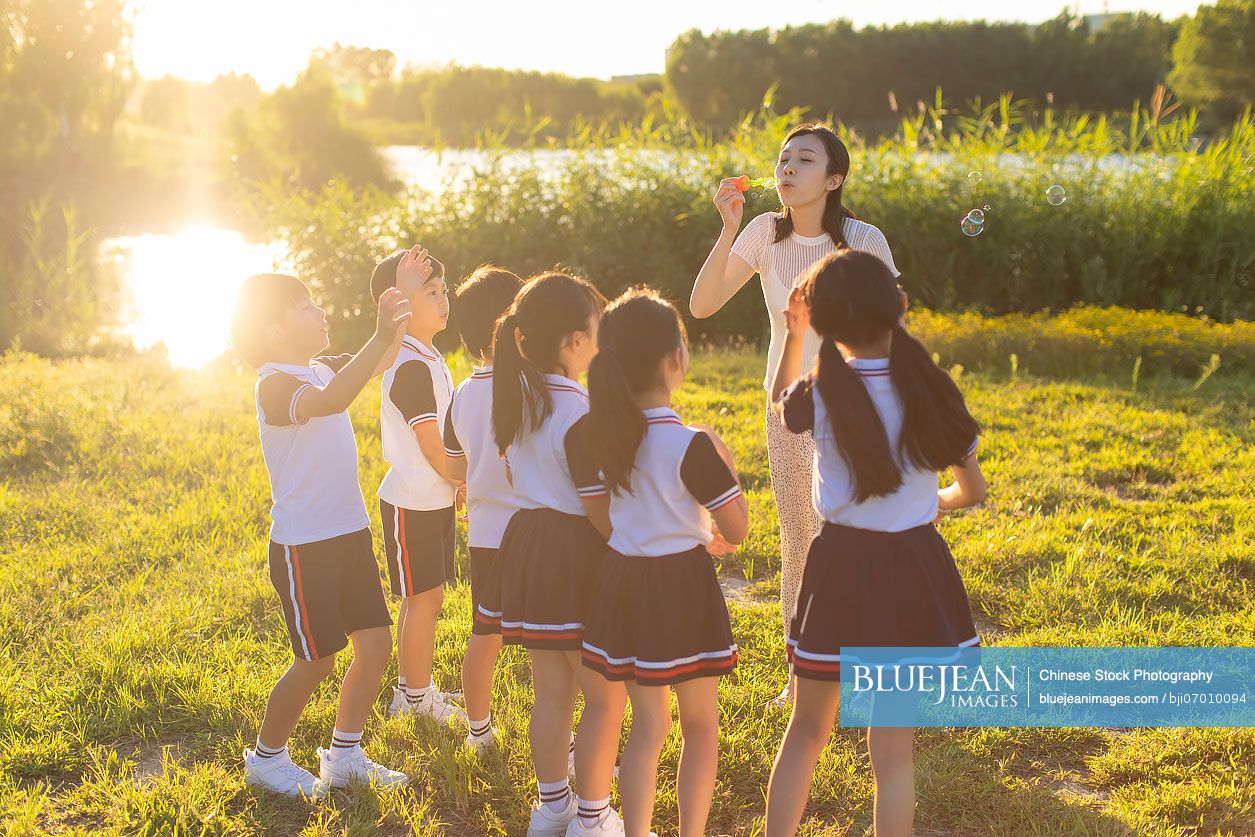 Cheerful Chinese school children and their teacher blowing bubbles on ...