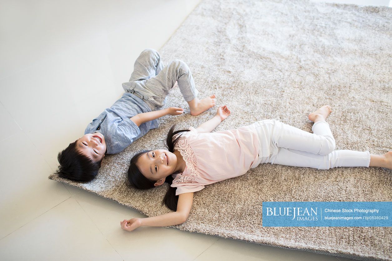 Cute Chinese children lying on carpet in new house