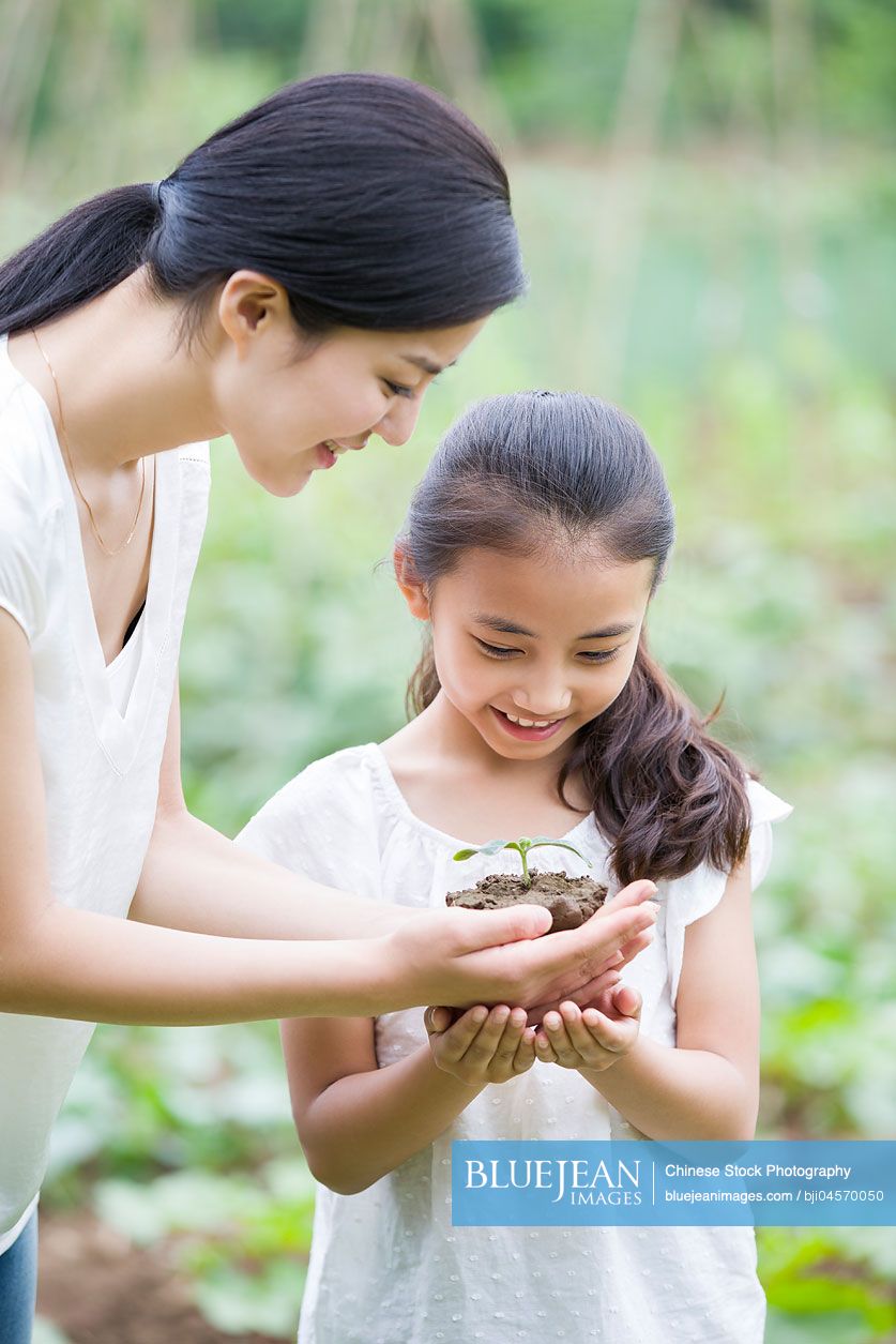 Young Chinese mother giving daughter a seedling
