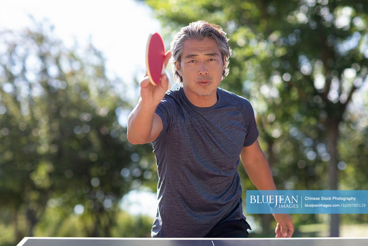 Happy mature Chinese man playing table tennis outdoors