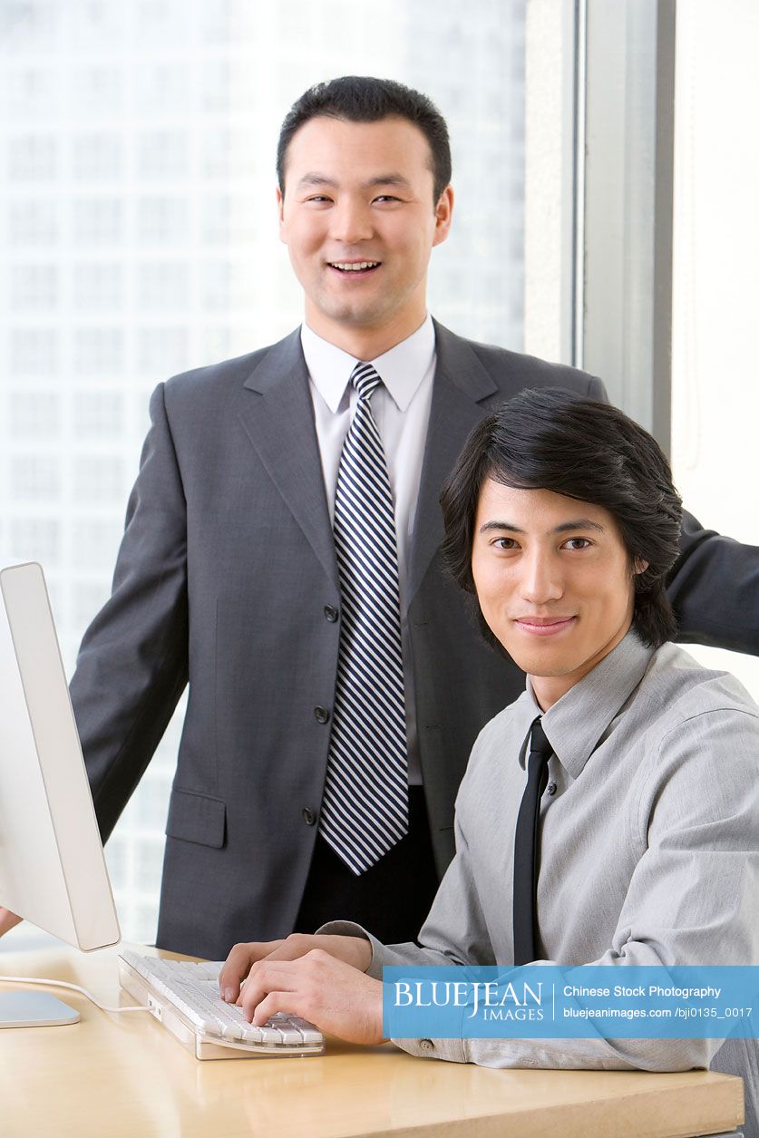 Chinese man in business suit shows young employee something on a computer
