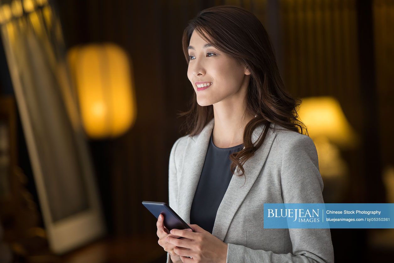 Cheerful young Chinese businesswoman holding a smart phone