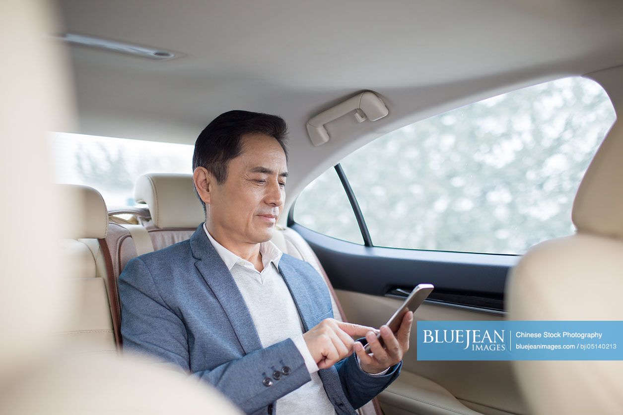 Chinese businessman using smart phone inside car