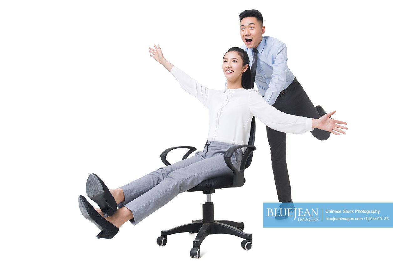 Chinese businessman pushing businesswoman in rolling office chair