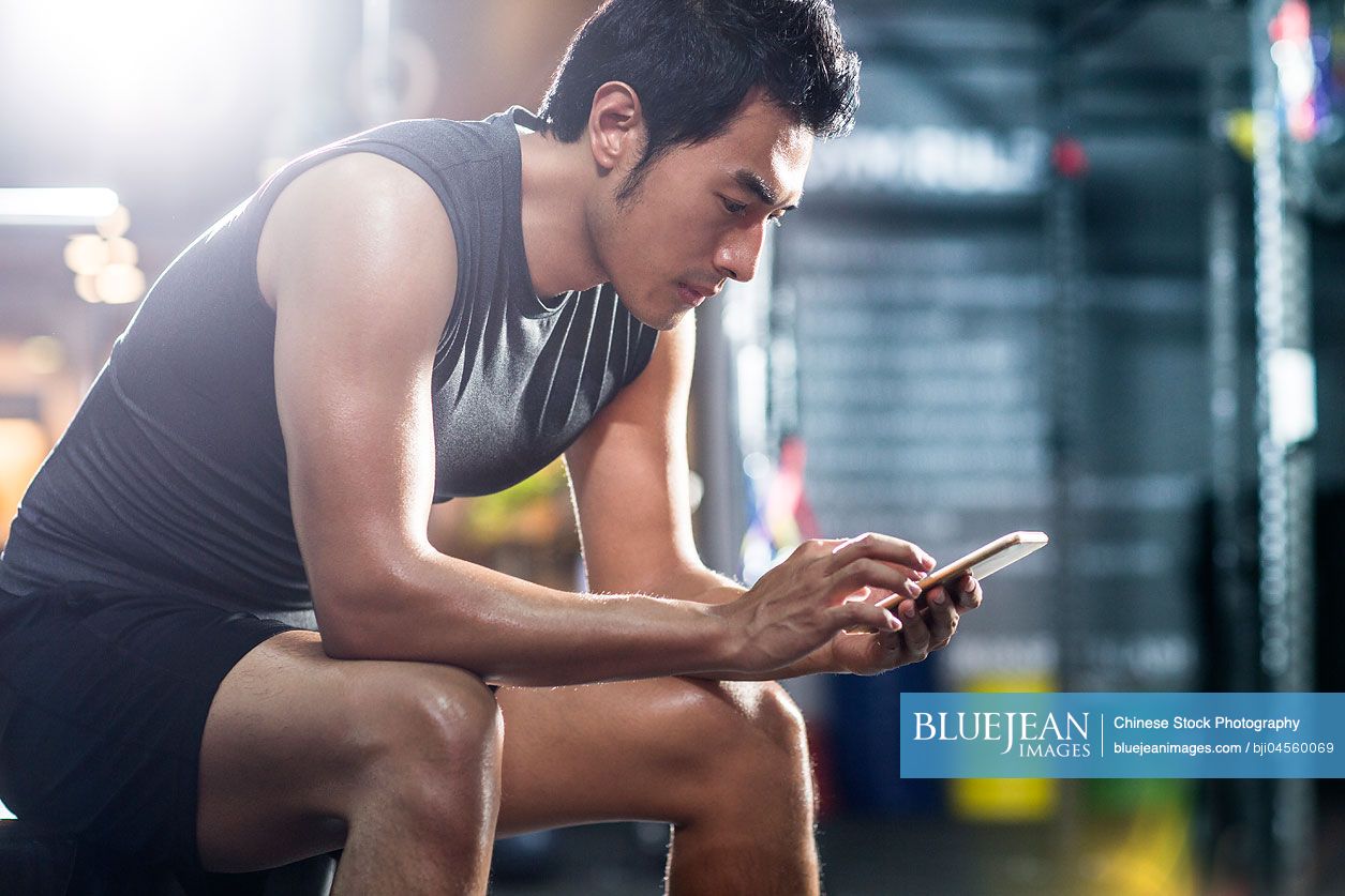 Young Chinese man using smart phone in gym