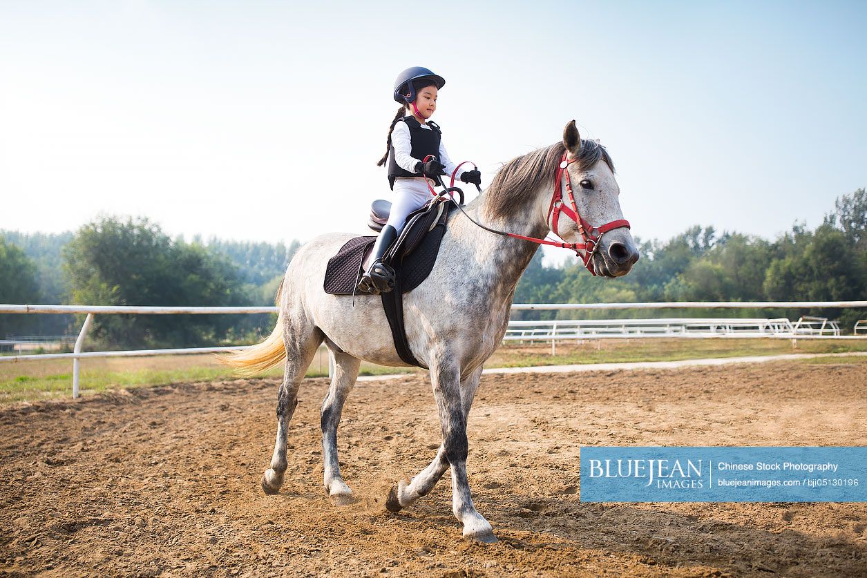 Cheerful little Chinese girl riding horse
