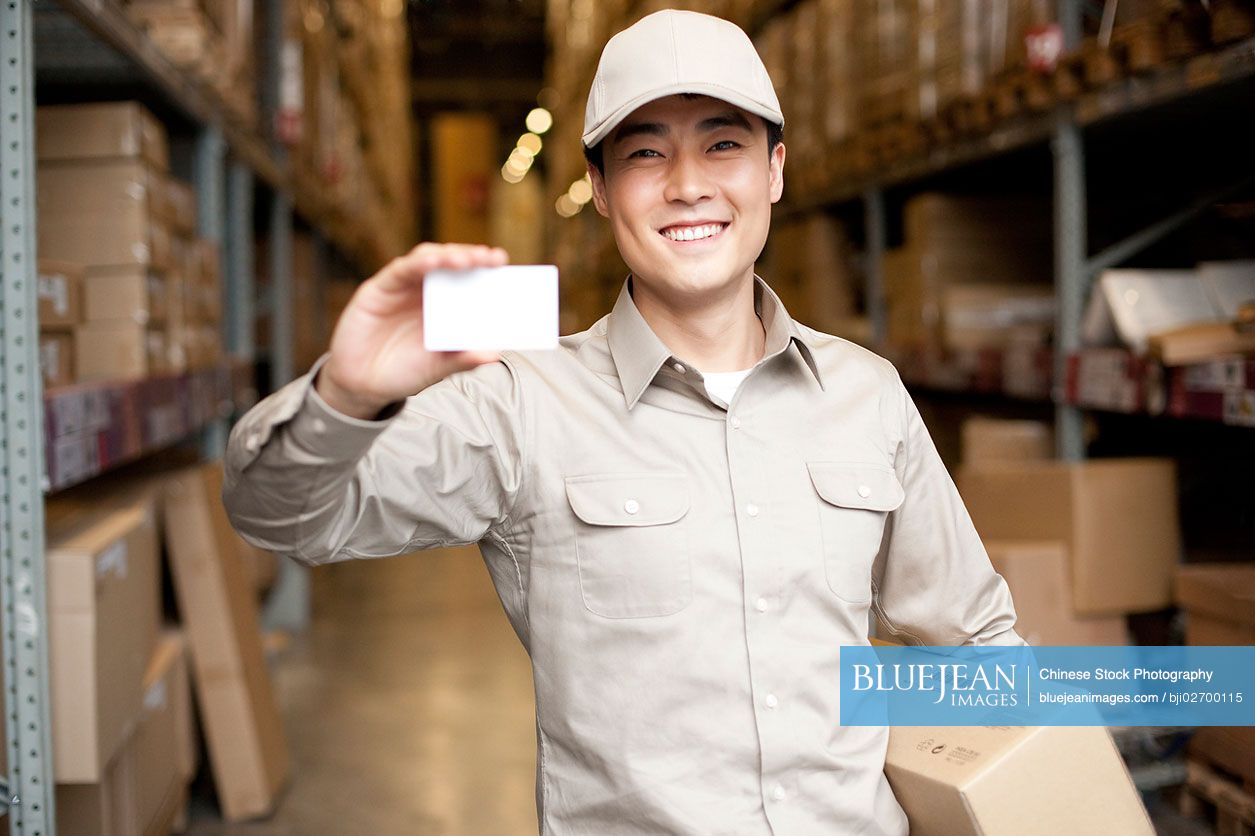 Male Chinese warehouse worker holding up a blank business card