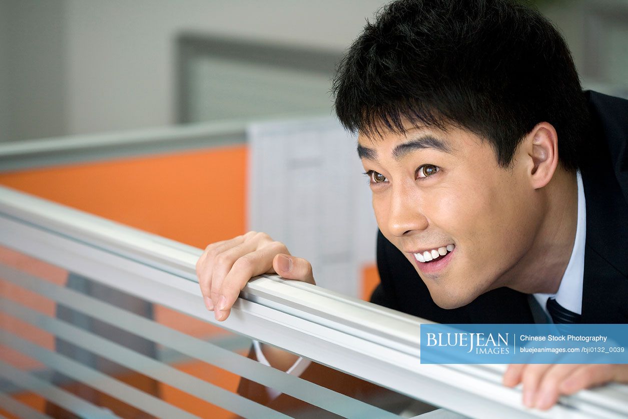 Chinese man peeking out from cubicle