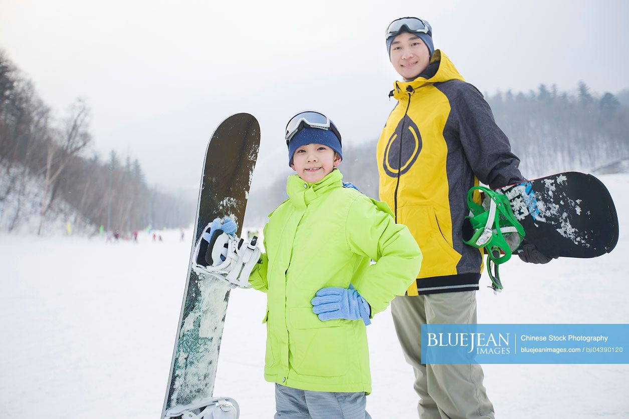 Young Chinese father and son with snowboards on the snow