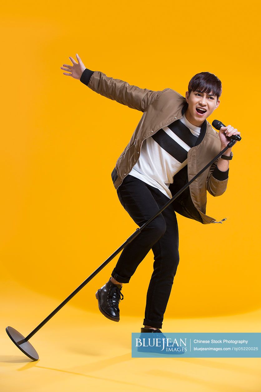 Cheerful young Chinese man singing with microphone