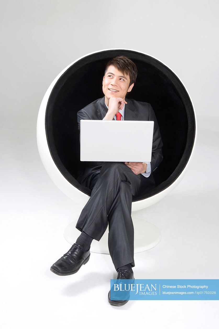 Young Chinese businessman using a laptop in a ball chair