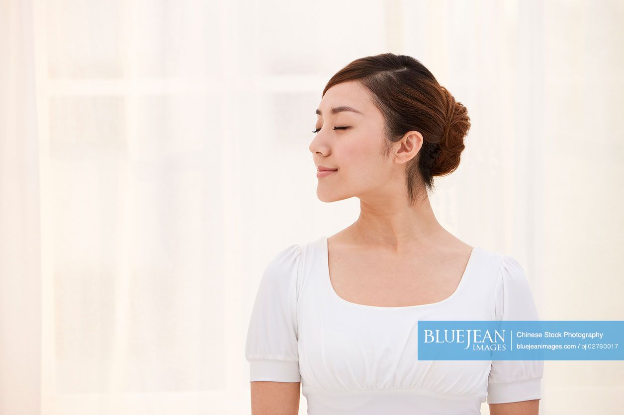 Young Chinese woman with her eyes closed and looking calm by the window