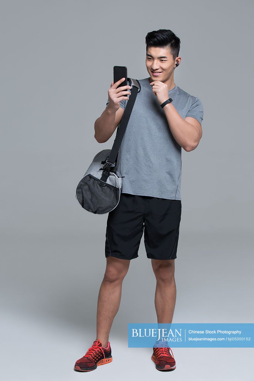 Cheerful young Chinese male athlete using smart phone