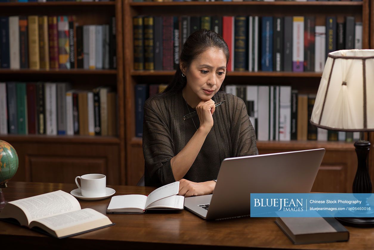 Elegant mature Chinese woman using laptop in study