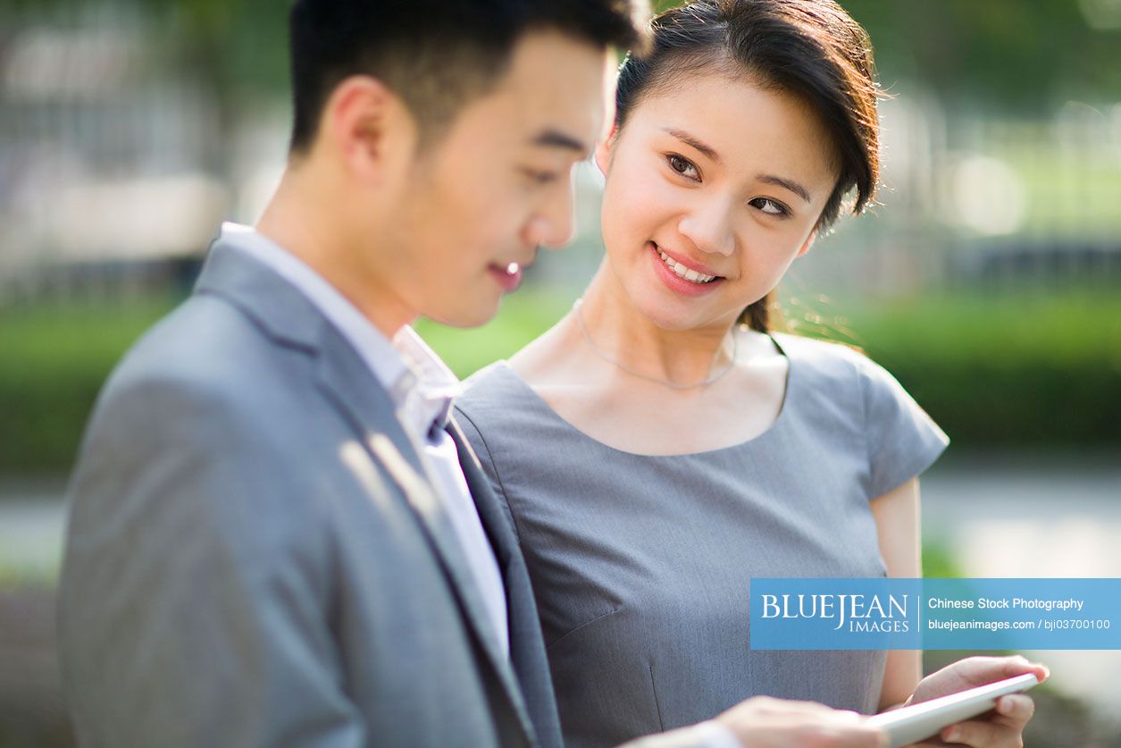 Happy Chinese businesspeople with digital tablet in discussion