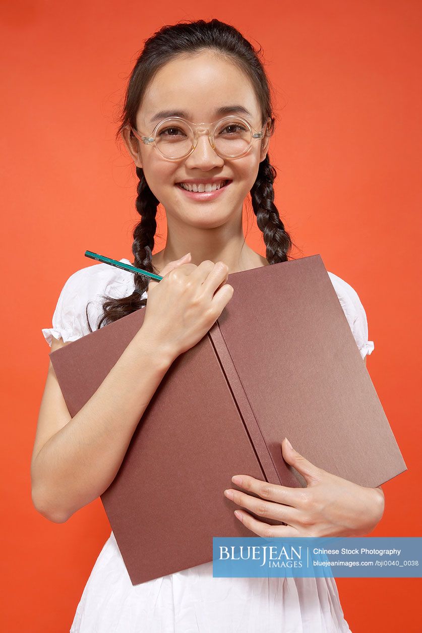 Young Chinese girl holding a book and pencil laughing