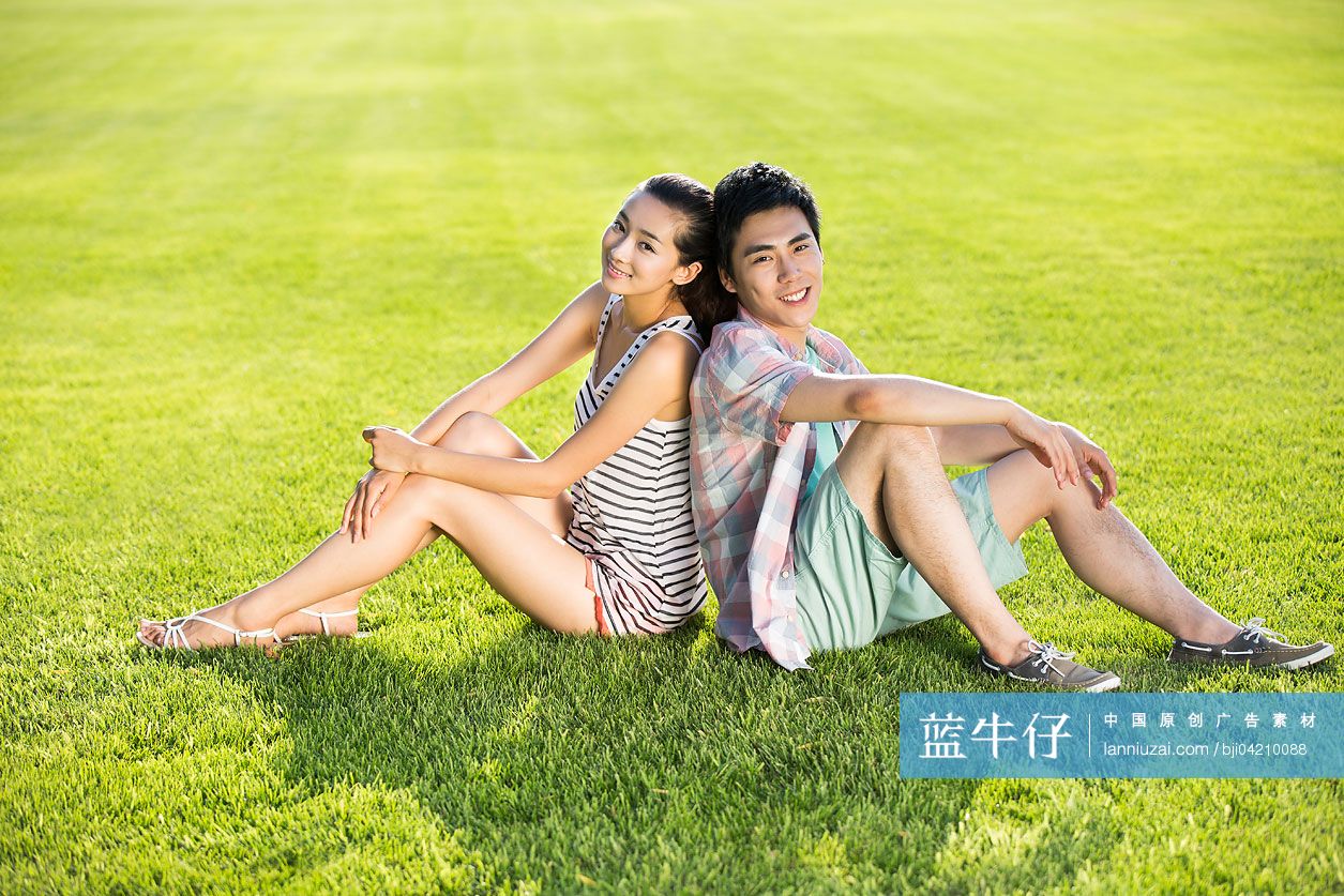 年轻情侣背靠背坐在草地上