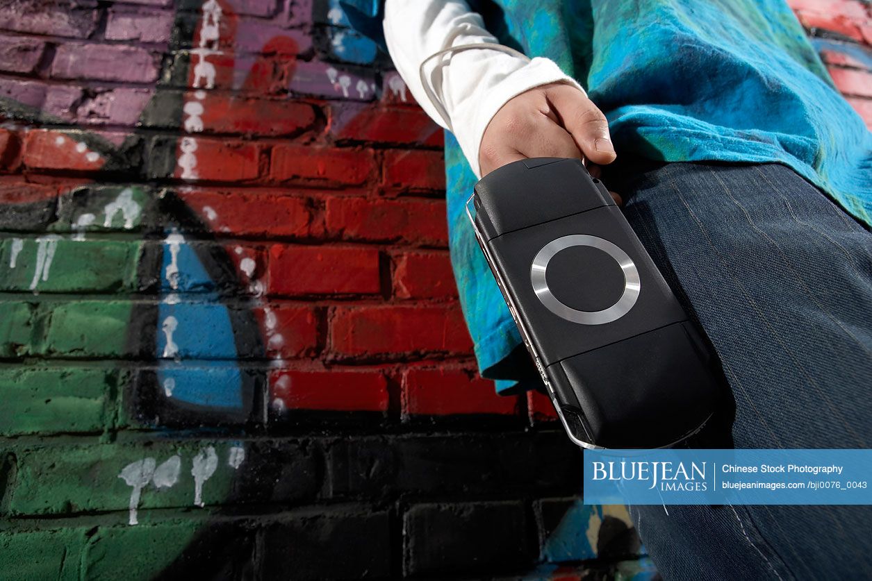 Chinese teenage boy holding personal game console