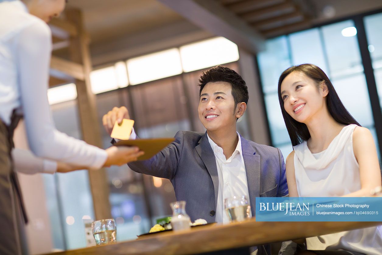 Young Chinese man paying bill by credit card in restaurant