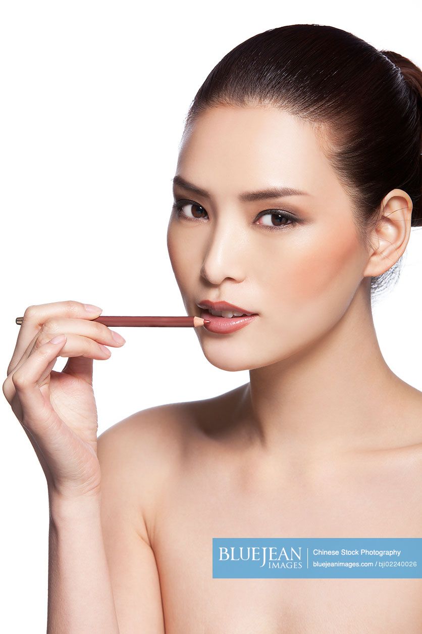 Headshot of young beautiful Chinese woman applying makeup