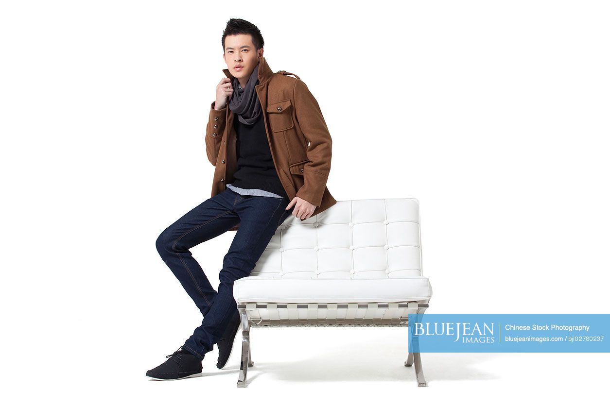 Stylish young Chinese man standing by chair