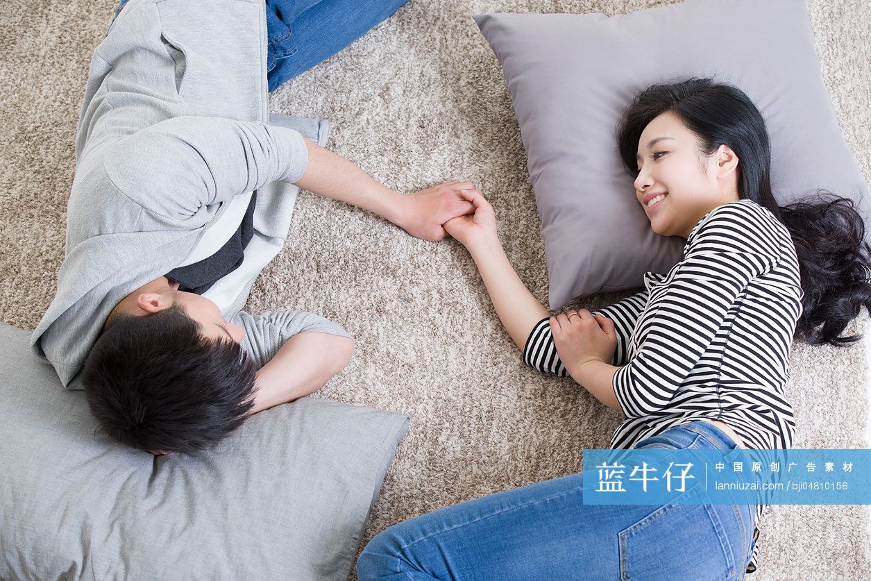 年轻情侣手牵手躺在地毯上