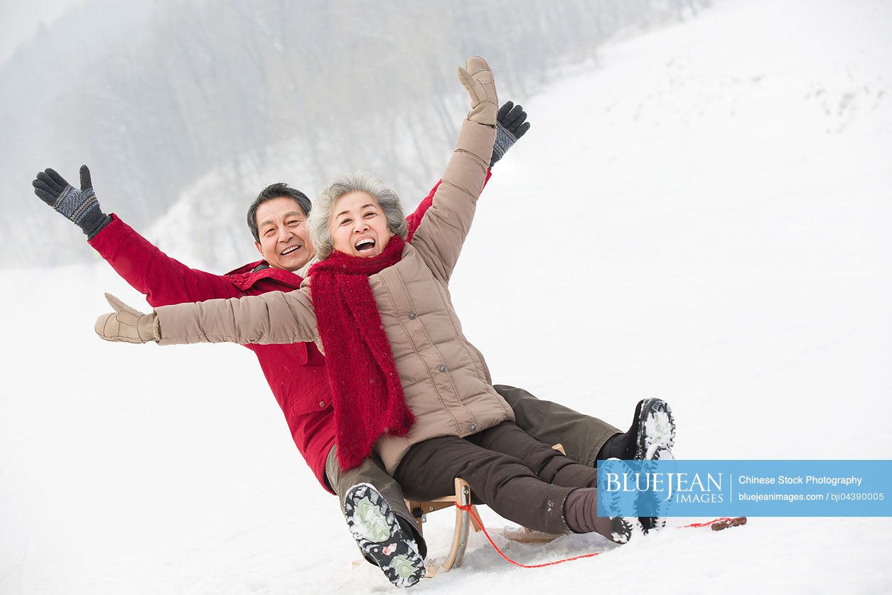 Happy senior Chinese couple sliding on a sled