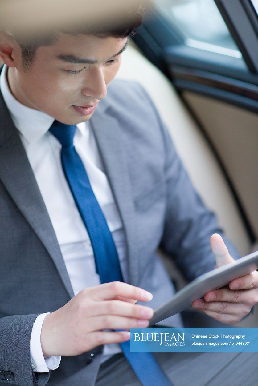 Chinese businessman using digital tablet in car back seat