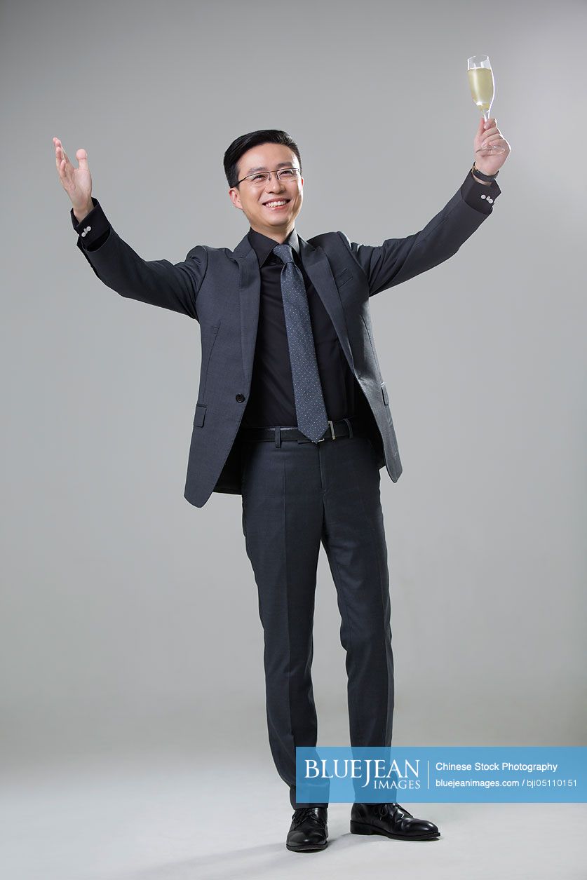 Cheerful mid adult Chinese businessman holding a glass of champagne